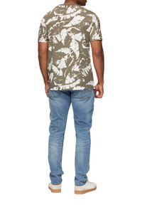 Camiseta de manga corta color oliva con estampado de hojas blancas, combinada con jeans de mezclilla azul claros y zapatillas blancas. Vista trasera del conjunto.