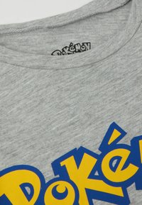Graues Baumwoll-T-Shirt mit einem auffälligen blauen und gelben "Pokémon"-Logo. Der Kragen ist im klassischen Rundhalsstil mit ordentlichem Nähen.