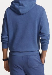Felpa con cappuccio blu dalla texture morbida, con polsini a coste e una tasca sul retro dei pantaloni della tuta blu coordinati.