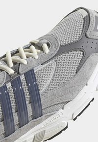 Sive tenisice za trčanje s mrežastim gornjim dijelom, tamnosivim plastičnim trotrakastim dizajnom, bijelim vezicama i teksturiranim gumeni potplat.