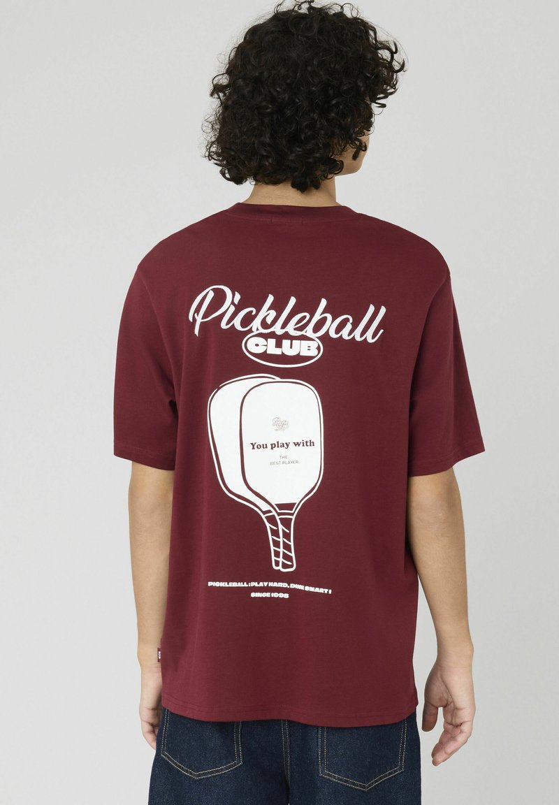 T-shirt en coton bordeaux avec un graphique blanc du Pickleball Club au dos, comprenant un design de raquette et des éléments textuels.