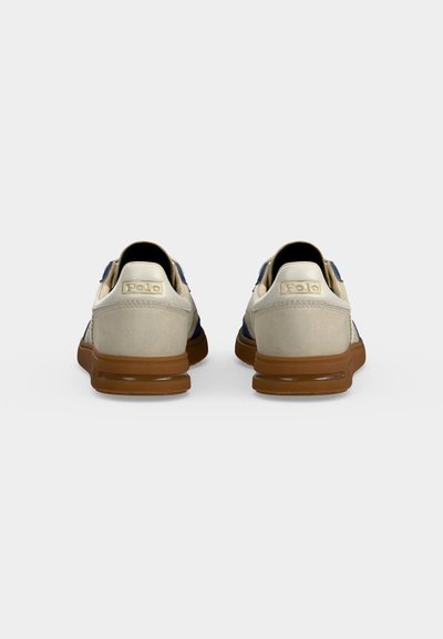 Ζευγάρι μπεζ και ναυτικό sneakers με καφέ σόλες, που φαίνονται από πίσω, με το λογότυπο "Polo" στις πίσω λωρίδες.