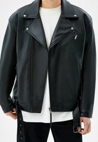 Svart konstläder motorcykeljacka med dragkedja, diagonal bröstficka och sidodragkedjor; har tryckknappar och justerbar bältdetalj.