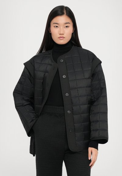 Musta tilava tikattu takki, jossa on suuret napit ja leveät hihat. Valmistettu sileästä kankaasta minimalistisella muotoilulla.