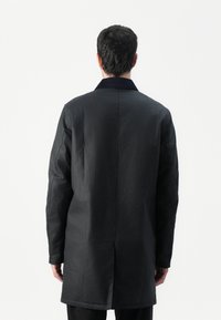 Manteau noir avec une texture lisse, manches longues et un col. Le dos présente une coupe droite et des détails minimaux.