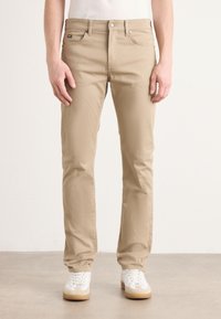 Beige katoenen broeken met een rechte pijpdesign, voorzien van voorzakken en een ritssluiting, gecombineerd met witte sneakers met licht beige zolen.