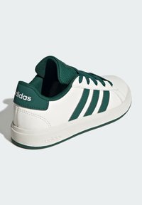 White leather sneaker with green accents, textured green collar, and three green stripes. Features a textured white rubber sole.