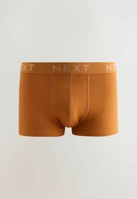 Vīriešu oranžas kokvilnas bokseršorti ar mīkstu jostas joslu, uz kuras gaiši rozā krāsā redzams zīmola nosaukums "NEXT". Gluda tekstūra, piegulošs dizains.