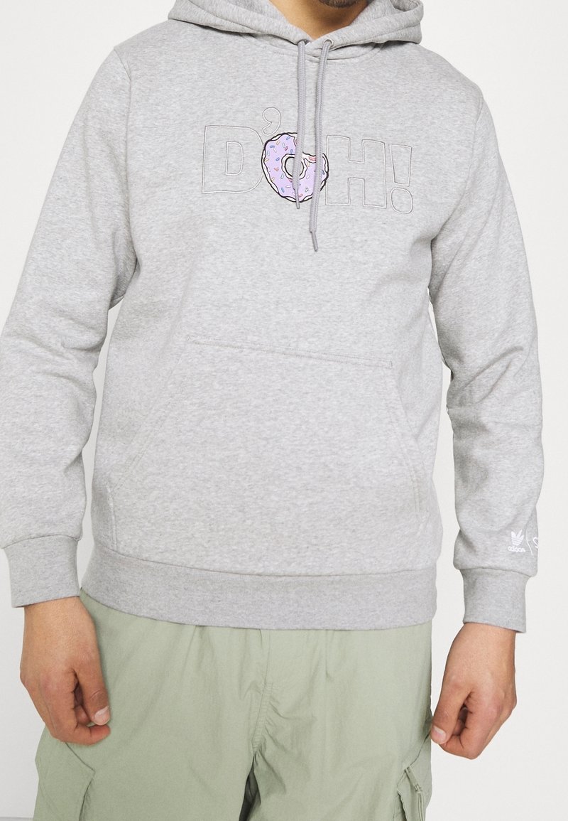 Grå hoodie i bomullsblandning med en ficka fram, med texten "D'OH!" och en donutgrafik. Mudden på ärmarna och fållen är ribbade.