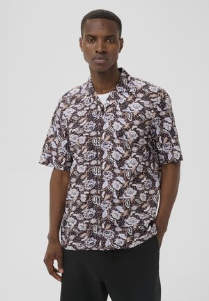 Man draagt een kortärmelig overhemd met een bruin, wit en lichtblauw bloemenpatroon, gecombineerd met een zwarte broek.