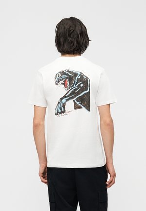 Person with dark hair wearing a white t-shirt featuring a large, roaring black panther graphic on the back, paired with black pants.