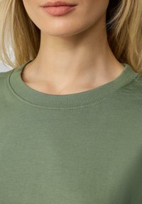 Oliwkowy bawełniany sweter z okrągłym, ściąganym dekoltem. Miękka tekstura o gładkiej powierzchni, z wyraźnym szwem wokół kołnierza.
