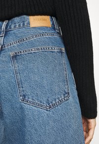 Vaaleansiniset farkut korkealla vyötäröllä, joissa on nahkainen etiketti "WEEKDAY" takana. Sisältää takataskun ompeluyksityiskohdilla.