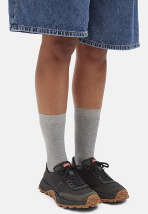 Legs wearing gray mid-calf socks, black and brown sneakers with laces, and knee-length blue denim shorts against a white background.