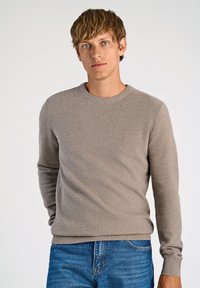 Suéter texturizado gris claro con cuello redondo y mangas largas, combinado con jeans de mezclilla azules. Tejido suave en un diseño ajustado.