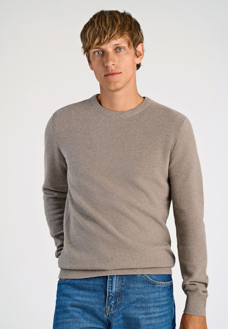 Suéter texturizado gris claro con cuello redondo y mangas largas, combinado con jeans de mezclilla azules. Tejido suave en un diseño ajustado.