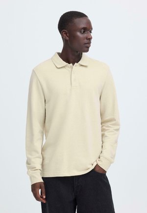 Beiges Poloshirt mit langen Ärmeln, Kragen, Drei-Knopf-Leiste und weicher Textur, kombiniert mit schwarzen Hosen. Sauberes, schlichtes Design.