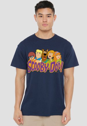 Man wearing navy blue t-shirt with colorful Scooby-Doo characters and large "SCOOBY-DOO!" text on front, standing against plain background.