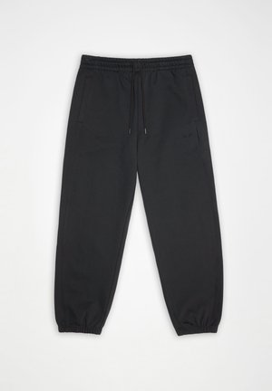 Svart joggebukse med elastisk midje, snor, sidelommer, elastiske mansjetter og subtil "HANS"-logo på venstre lår, lagt flatt på hvit bakgrunn.