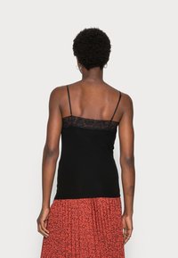 Svart linne med spetsdetalj vid halsen, med tunna justerbara band och ribbat mönster, kompletterat med en mönstrad röd kjol.