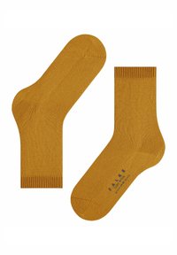 Una coppia di calzini in cotone giallo senape, uno steso piano, l'altro che mostra la suola con il testo del marchio stampato in lettere scure.