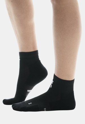 Chaussettes de sport noires avec des bords ribés, des talons et des orteils renforcés. Présentent une surface texturée et un logo blanc sur le côté.