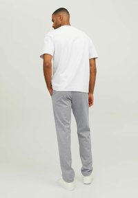 Weißes Baumwoll-T-Shirt mit kurzen Ärmeln, kombiniert mit hellgrauen Sweatpants. Weiße Sneakers vervollständigen das lässige Outfit. Rückansicht.