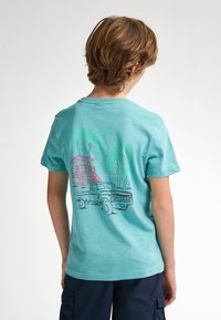 Tyrkysové bavlněné tričko s krátkými rukávy. Na zadní straně se nachází grafický design náklaďáku, plážové hlídky a palem v živých barvách.