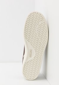 Semelle de chaussure de sport marron avec un dessous en caoutchouc blanc texturé présentant un motif de bande diagonale et affichant le logo "K-Swiss".