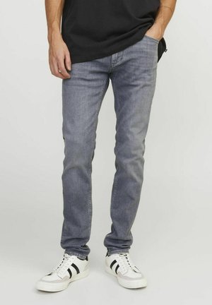 Szürke farmernadrág, slim fit szabású, egy hátsó zsebbel és minimális díszítéssel, fehér sportcipőkkel, fekete részletekkel.