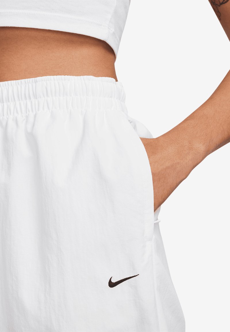 Pantaloni corti bianchi realizzati in tessuto leggero con vita elastica. Presentano una tasca laterale e un piccolo logo Nike nero sull'orlo.