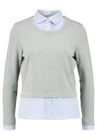 Felpa grigia con maniche lunghe indossata sopra una camicia a righe bianche e blu con colletto, caratterizzata da una scollatura arrotondata e orlo della camicia con bottoni.