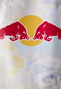Dres s brendom Red Bull s žutim kružnim logotipom i dva silueta crvenih bikova. Tkanina ima svijetloplavi apstraktni uzorak i mrežastu teksturu.