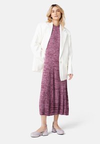 Blazer blanc sur une robe texturée, à mi-genoux, de couleur purpurine avec des plis. Chaussures à plateforme roses claires avec des brides de cheville. Esthétique simple et moderne.