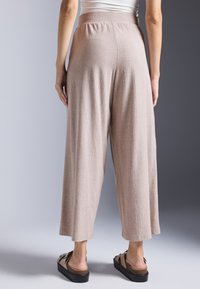 Světle růžové, ribbované široké kalhoty s elastickým pasem, dosahujícími do poloviny lýtek. V kombinaci s hnědými skládacími sandály, které mají texturovaný povrch.