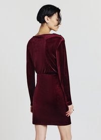 Burgunderrotes Samtkleid mit langen Ärmeln und figurbetonter Silhouette, ausgestattet mit einem tief ausgeschnittenen Rückenausschnitt und glatter Textur mit leichtem Glanz.