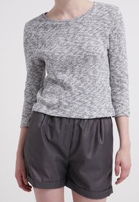Grau-weiß gemusterter Langarmtop, kombiniert mit dunkelgrauen, gefalteten Shorts, die einen lockeren Schnitt und einen umgeschlagenen Saum aufweisen.
