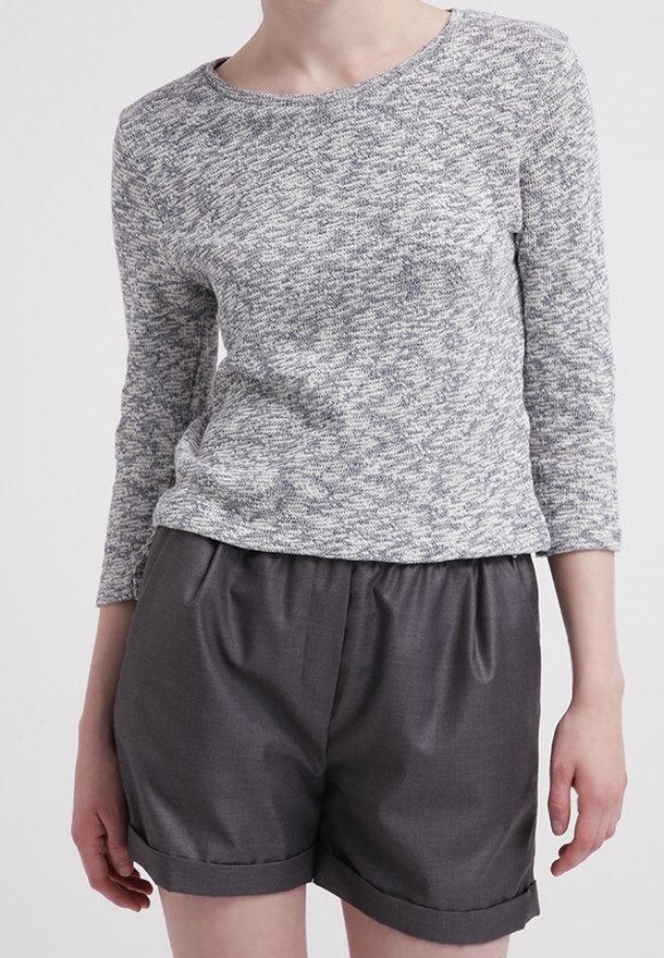Grau-weiß gemusterter Langarmtop, kombiniert mit dunkelgrauen, gefalteten Shorts, die einen lockeren Schnitt und einen umgeschlagenen Saum aufweisen.