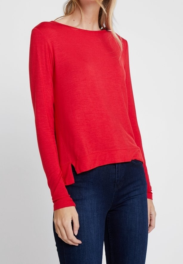 Rotes langärmliges Strickoberteil mit Bootsausschnitt, ausgestattet mit seitlichen Schlitzen am Saum, kombiniert mit dunkelblauen Jeans. Weiche Textur und leichtes Material.