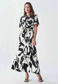 Čierno-biely vzorovaný maxi šaty s krátkymi rukávmi, predným zapínaním na gombíky a viazaním v páse. Vyrobené z ľahkého materiálu s voľným strihom.