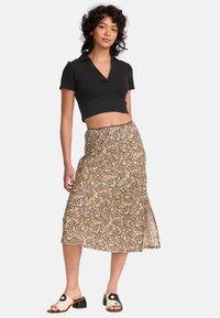 Haut cropped noir à manches courtes, associé à une jupe midi fluide à imprimé floral dans des couleurs pastel variées. Porté avec des sandales ivoire.