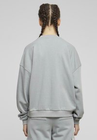 Sudadera gris claro con un ajuste relajado, hombros caídos, puños y cintura acanalados. Textura de tela suave, detalles de costura mínimos.