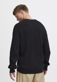 Pulover negru din țesătură cu nervuri, cu mâneci lungi și guler rotund, având un material texturat. Spatele prezintă o croială lejeră și umeri puțin căzuți.