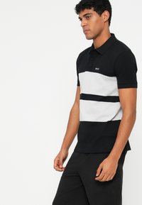 Black and gray striped polo shirt with a classic collar, featuring a small "BOSS" logo on the chest, paired with black pants.