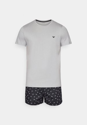 Graues Baumwoll-T-Shirt mit Rundhalsausschnitt und kurzen Ärmeln, kombiniert mit schwarzen Badehosen, die ein weißes wiederholtes Logo-Muster aufweisen.