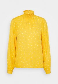 Gul blus med långa ärmar, hög volangkrage och vita prickar. Tillverkad av lättviktig tyg med en strukturerad yta.