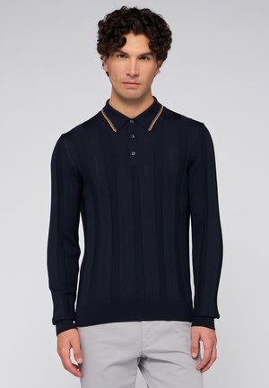 Camisa polo de manga larga en color marino con textura de canalé, corte ceñido, cuello y botones en contraste color tostado, y con rayas verticales en todo su diseño.