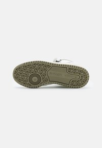 Sneaker sole with a patterned design, featuring a light beige rubber material and embossed branding. Circular and linear traction elements visible.