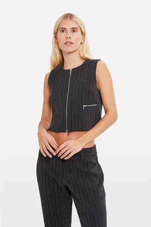 Lyhyt musta hihaton liivi, jossa valkoisia pystysuoria raitoja, jossa on etuvetoketju ja koristeellinen vetoketjupussi vasemmalla puolella.