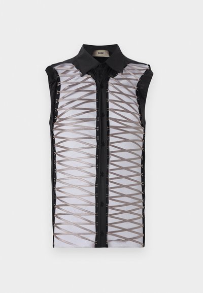 Musta hihaton paita, jossa on läpinäkyvä etuosa ristikkäisillä hihnoilla, napitus ja muotoiltu kaulus.